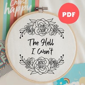 May include: A black and white embroidery pattern featuring a floral design with the text "The Hell I Won't". The pattern is displayed in a wooden embroidery hoop.