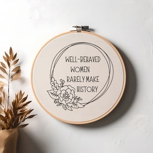 Puede incluir: Un bastidor de bordado redondo con el texto negro "WELL-BEHAVED WOMEN RARELY MAKE HISTORY". El dise&ntilde;o incluye una ilustraci&oacute;n floral y de hojas. El bastidor es de madera y la tela es de color beige claro.
