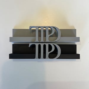 Peut inclure: Présentoir à trois niveaux avec les lettres "TPD" dans une police stylisée. Les étagères sont noires, grises et gris clair. Les lettres sont d'une couleur gris clair. Les étagères sont empilées les unes sur les autres.