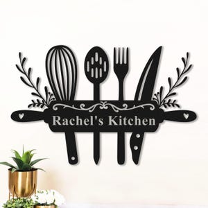 May include: Black metal kitchen sign featuring a rolling pin with a whisk, slotted spoon, fork, and knife. The sign reads "Rachel's Kitchen" in a decorative font, with floral accents and heart details.