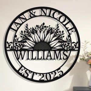 Könnte beinhalten: Rundes Schild aus schwarzem Metall mit dem Text "Jan & Nicole Williams Est 2025" und einer Sonnenblume mit Blättern in der Mitte.