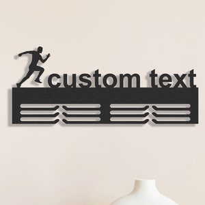 May include: Black metal running-themed wall art with the words "custom text". A silhouette of a runner is positioned above the text. Below the text are three horizontal bars with slots for displaying medals. A decorative item.
