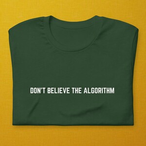May include: A dark green t-shirt with the text "DON'T BELIEVE THE ALGORITHM" printed in white on the front.