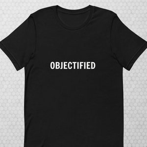 Puede incluir: Camiseta negra con la palabra "OBJECTIFIED" impresa en blanco en la parte delantera.