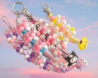 May include: A set of five colorful beaded keychains with different charms. The keychains are made with pink, white, purple, and blue beads. The charms include a yellow bear, a black and white penguin, and a pink and white character.