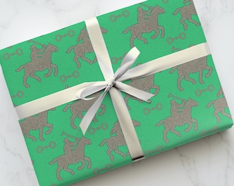 May include: Gift-wrapped present with green paper featuring a repeating pattern of polo players on horseback in a brown line design. The gift is tied with a silver ribbon and bow.