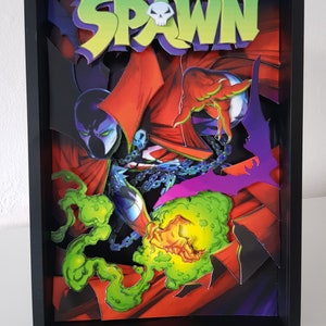 May include: A framed 3D pop-up art piece featuring the comic book character Spawn. The image is set against a red and black background with green and purple accents. The title "Spawn" is featured in large letters at the top of the frame.