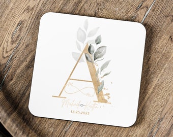 May include: White square coaster with a gold letter A surrounded by green and gray watercolor leaves. The text "Mr. & Mrs. Michael Kaitlin 12.25.2023" is printed below the letter.