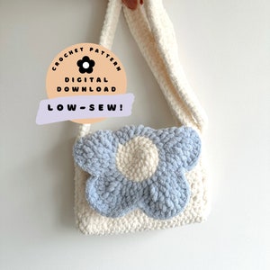 May include: A cream-coloured, crocheted shoulder bag with a large, light blue and cream flower appliqué. The bag has a long strap and the text "CROCHET PATTERN DIGITAL DOWNLOAD LOW-SEW!" is on a circular sticker.