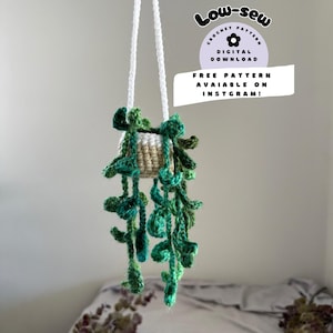May include: A crocheted hanging plant with green leaves and a beige pot. The plant is hanging from a white string. The image includes the text "Low-sew Crochet Pattern Digital Download Free Pattern Available on Instagram!"
