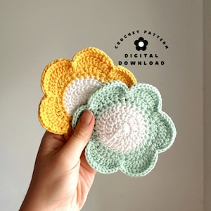 May include: Two crocheted flower coasters, one yellow and one green, with white centres. The coasters are held in a hand. The text "Crochet Pattern Digital Download" is visible in the image.