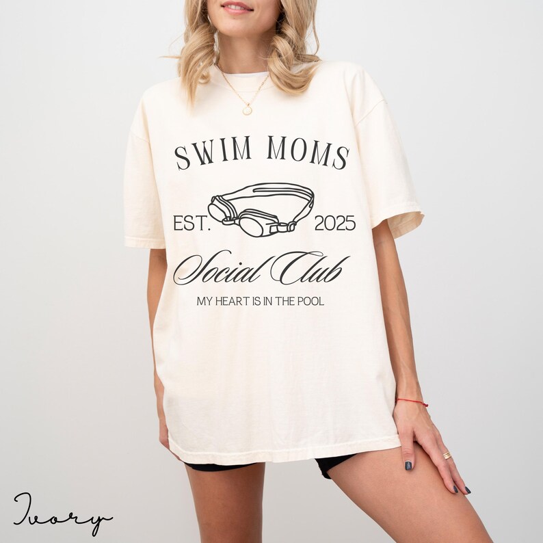 Puede incluir: Una camiseta de manga corta color marfil con texto en negro que dice SWIM MOMS EST. 2025 Social Club MY HEART IS IN THE POOL, con una ilustraci&oacute;n lineal de unas gafas de nataci&oacute;n centrada entre los elementos de texto.