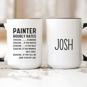 May include: White ceramic mug with a black handle and rim. The mug has black text that reads "PAINTER HOURLY RATES $100/HR...STANDARD $180/HR...IF YOU WATCH $200/HR...IF YOU HELP $300/HR...IF YOU WORKED ON IT FIRST $500/HR...IF YOU TELL ME HOW TO DO MY JOB". The other mug is white with a black handle and rim. The mug has black text that reads "JOSH".