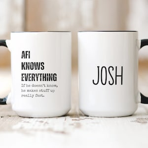 May include: Two white ceramic mugs with black handles. The mug on the left has the text "AFI KNOWS EVERYTHING If he doesn't know, he makes stuff up really fast." The mug on the right has the text "JOSH".