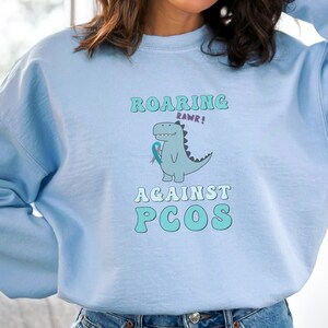 PCOS Sweatshirt, Dinosaur Roaring Against PCOS Sweater, PCOS Awareness Chronic Illness Teal Ribbon Gift For Wife, Women, Mother's Day Gift