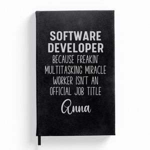 May include: Black leather-bound journal with the text "SOFTWARE DEVELOPER because freakin' multitasking miracle worker isn't an official job title Anna" in white lettering.