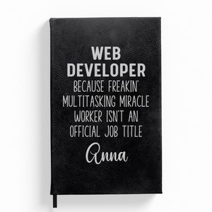 May include: Black leather-bound journal with the text "WEB DEVELOPER because freakin' multitasking miracle worker isn't an official job title Anna" in white lettering.