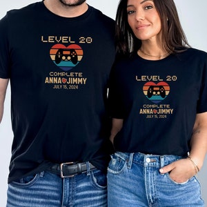 May include: Two black t-shirts with a retro video game controller graphic and the text "Level 20 Complete Anna Jimmy July 15, 2024".