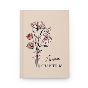 May include: A beige journal with a floral illustration of pink and red flowers with a pink bow. The text "Anna Chapter 18" is printed below the illustration.