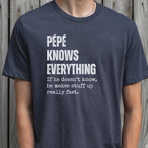 May include: Dark blue t-shirt with the text "PÉPÉ KNOWS EVERYTHING" in white block letters. Below the main text is the phrase "If he doesn't know, he makes stuff up really fast."
