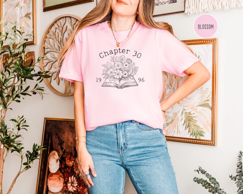 May include: A light pink t-shirt with the text "Chapter 30" above a floral design and the numbers "1996". The shirt is paired with blue jeans. The word "Blossom" is in a pink circle in the upper right corner.