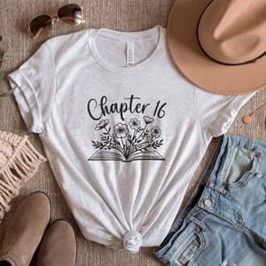 May include: A gray t-shirt with the text "Chapter 16" and a black and white illustration of a book with flowers.