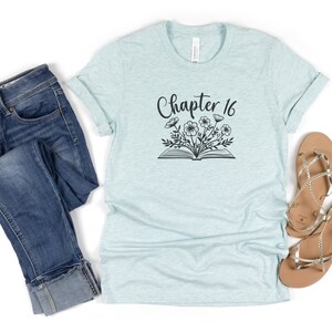 May include: A light blue t-shirt with the text "Chapter 16" and a black and white illustration of an open book with flowers growing from it.
