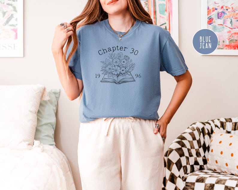 May include: A blue jean-colored t-shirt with the text "Chapter 30" above a floral and book graphic. The numbers "1996" and "19" are below the book. The shirt is a comfortable, casual style.