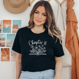 May include: Black t-shirt with white text that says "Chapter 16" and a graphic of a book with flowers coming out of it.