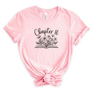 May include: Pink t-shirt with a black graphic of an open book with flowers and the text "Chapter 16".