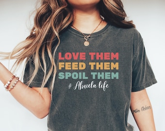 May include: Dark gray t-shirt with the text "LOVE THEM FEED THEM SPOIL THEM # Abuela life" in red, yellow, and teal lettering. The shirt is a crew neck style.