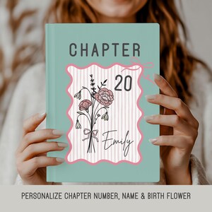 May include: A teal-colored book with the word "CHAPTER" at the top. The cover features a pink and white floral design with the number "20" and the name "Emily". The book is held by a person.