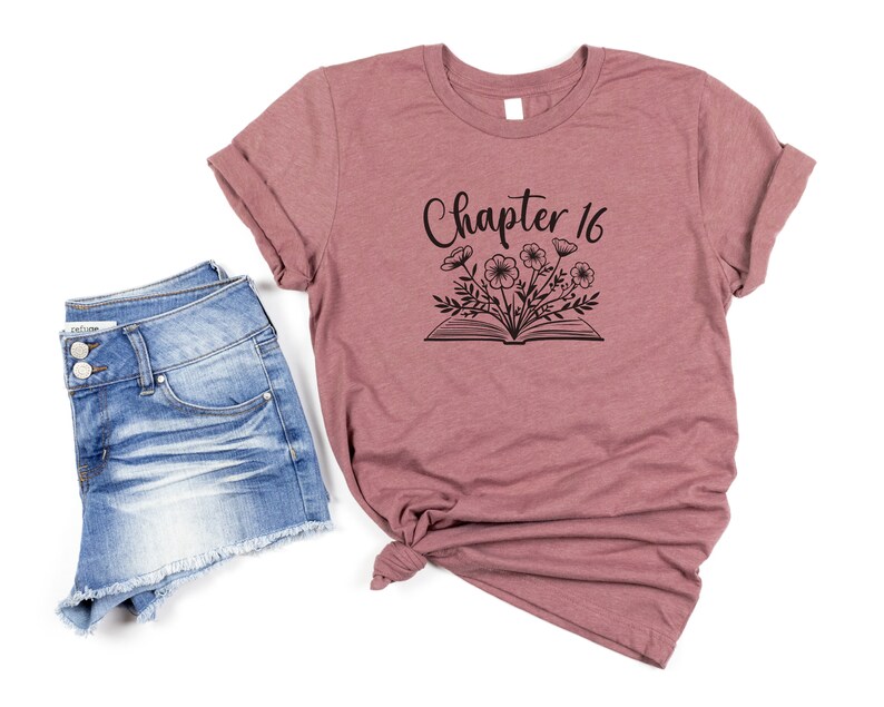 May include: A mauve t-shirt with the text "Chapter 16" and a black and white illustration of a book with flowers on top.