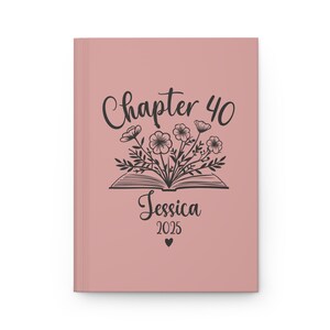 May include: A blush pink journal cover with a black illustration of an open book with flowers growing out of it. The text "Chapter 40" is above the book and the text "Jessica 2025" is below the book.