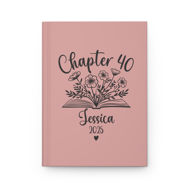 May include: A blush pink journal cover with a black illustration of an open book with flowers growing out of it. The text "Chapter 40" is above the book and the text "Jessica 2025" is below the book.