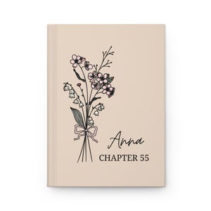 May include: A beige journal with a floral illustration of pink flowers and green leaves. The text "Anna Chapter 55" is printed on the front.