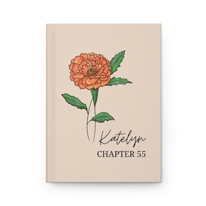 May include: A beige journal with an orange marigold flower illustration and green leaves. The journal cover has the name "Katelyn" in script and the text "CHAPTER 55" in a serif font.
