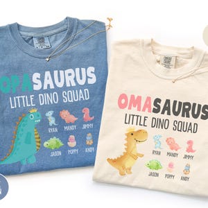 May include: Two t-shirts, one blue and one ivory, with dinosaur graphics. The blue shirt says "Opa Saurus Little Dino Squad" with dinosaur illustrations and names. The ivory shirt says "Oma Saurus Little Dino Squad".