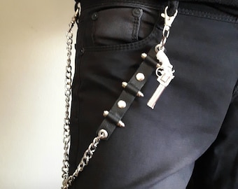 May include: A silver chain with a black leather strap and a silver toy gun charm. The chain is attached to a belt loop on a pair of black jeans.