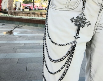 May include: Black metal cross and chain accessory attached to light-colored jeans. The cross is ornate, and the chain hangs in multiple strands. A stylish, edgy accessory.