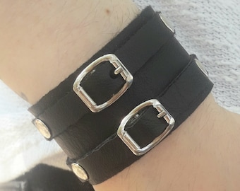 May include: A black leather bracelet with two silver buckles and silver studs.