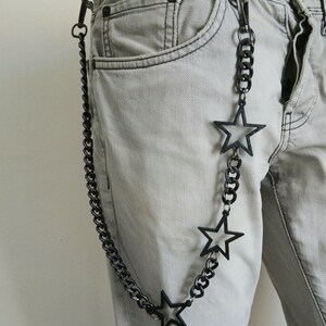 May include: A black chain with three star-shaped charms hangs from a belt loop on a pair of light gray jeans.