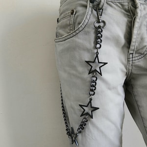 May include: A black chain with star-shaped charms attached to it. The chain is hanging from a belt loop on a pair of light gray jeans.