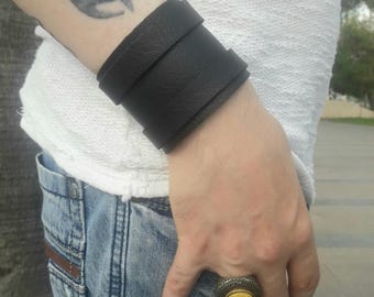 May include: A wide black leather cuff bracelet with a textured surface.