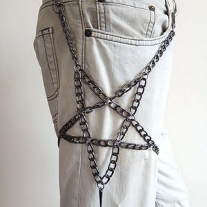 Puede incluir: Un accesorio de cadena plateada con un dise&ntilde;o de estrella de cinco puntas. La cadena est&aacute; sujeta a una trabilla y cuelga por la pierna, con una punta en la parte inferior de la estrella. El accesorio se lleva sobre unos vaqueros claros.