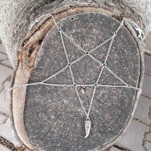 May include: A silver chain body jewelry piece with a pentagram design and a silver fang pendant.