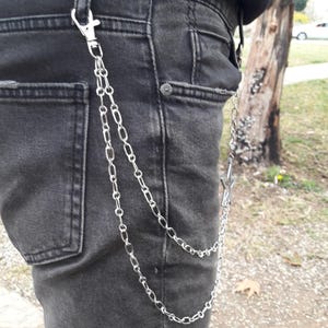 May include: A silver chain with a star-shaped charm attached to a belt loop. The chain is double-layered and hangs down to the wearer's thigh.