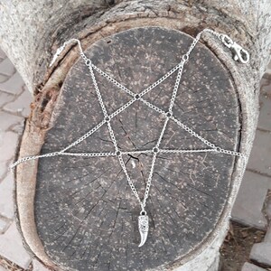 May include: A silver chain body jewelry piece with a pentagram design and a silver pendant shaped like a fang.