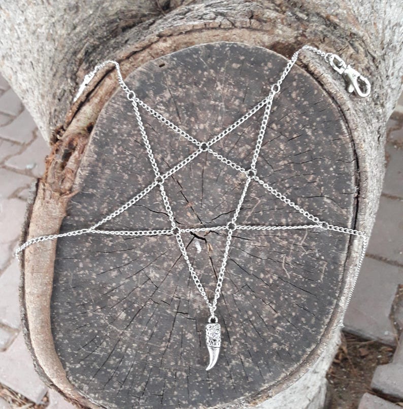 May include: A silver chain body jewelry piece with a pentagram design and a silver pendant shaped like a fang.