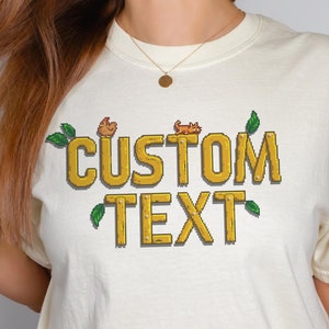 Comfort Colors gamer t-shirt in pixel art style, inspired by Stardew Valley. Customizable with your own text. Soft, retro style perfect for gamers and casual wear